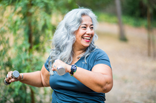 Woman walking on a trail, smiling while holding hand weights